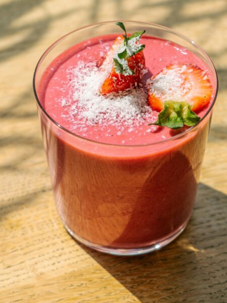 Refreshing strawberry smoothie topped with coconut flakes in natural light on a wooden table.